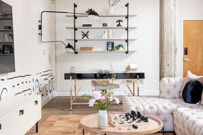 A modern living room with a round coffee table, a sofa, a TV mounted on the wall, and a bookshelf with various items.