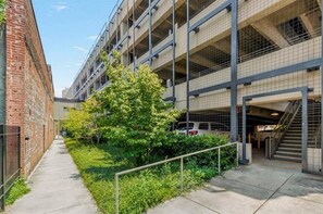 Un parking à plusieurs niveaux, avec un bâtiment en briques sur la gauche et une structure moderne dotée d’un escalier sur la droite.
