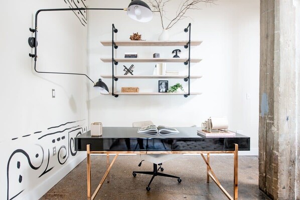 A modern office space with a black desk, a white wall with abstract art, and a metal shelving unit with decorative items.