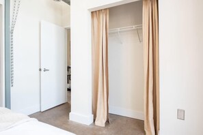 A bedroom with a bed, a closet with beige curtains, and a white door.