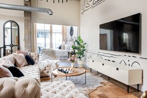 A modern living room with a large TV, a tufted sofa, a coffee table with chess pieces, and a large window with a view of the city.