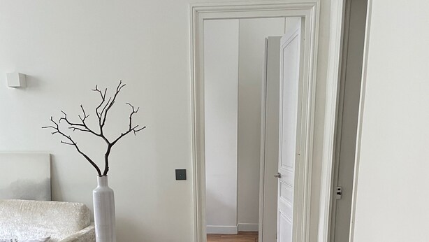 A modern living room with a wooden floor, a white sofa, a black coffee table with a book and a vase, and a decorative branch in a white vase. - Appartement indépendant Tour Eiffel/ Invalides (Paris)