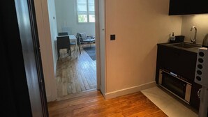 A kitchen with a built-in oven and microwave, wooden flooring, and a window providing natural light. - Appartement indépendant Tour Eiffel/ Invalides (Paris)
