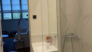 A modern bathroom with a glass shower enclosure, a white sink, and a handheld showerhead. - Appartement indépendant Tour Eiffel/ Invalides (Paris)