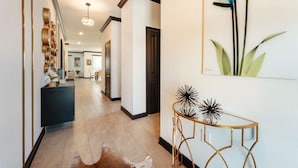 Un pasillo con una consola azul oscuro, una mesa de centro de vidrio con patas doradas y un cuadro grande con motivos florales en la pared.