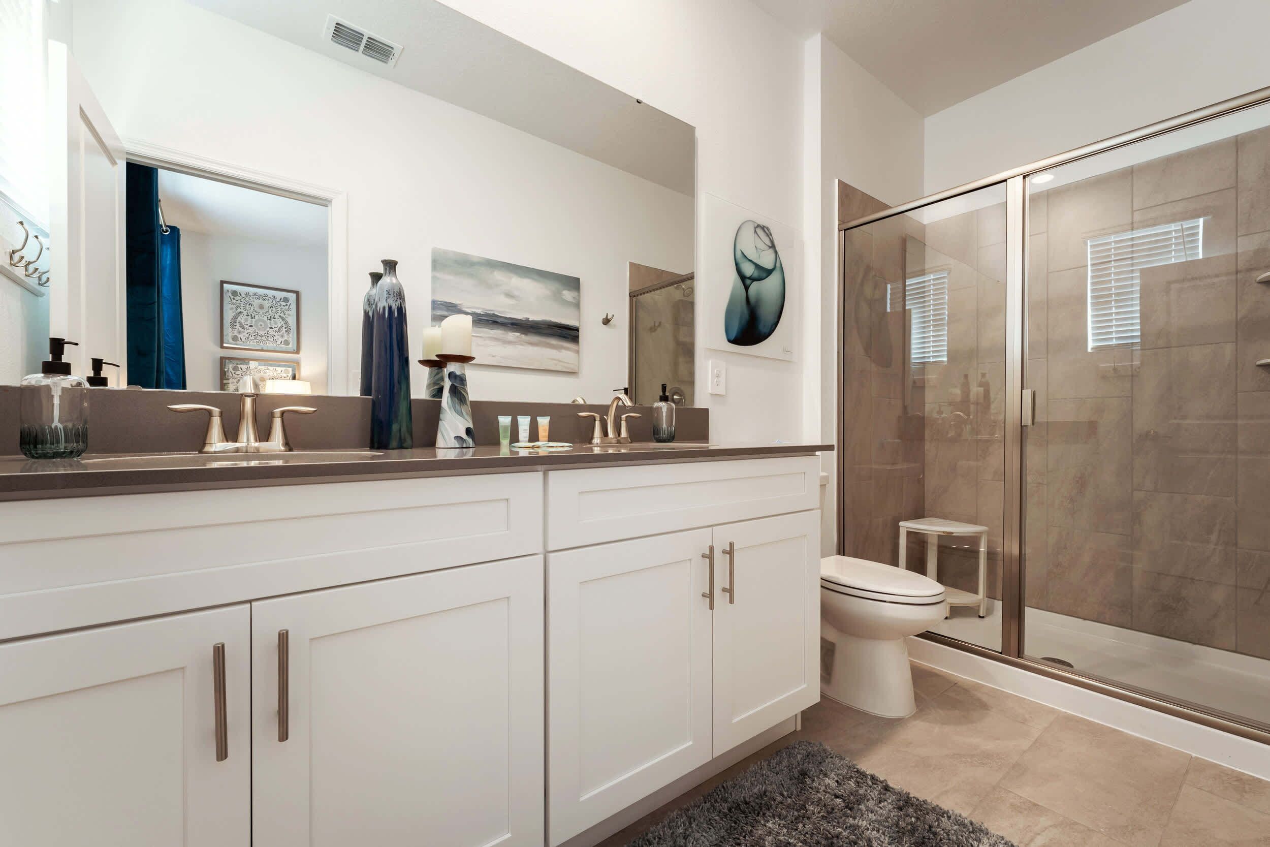 A modern bathroom with a glass shower enclosure, a white toilet, and a large mirror above the sink.