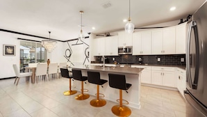 Una cocina moderna con armarios blancos, un refrigerador de acero inoxidable y una barra con cuatro taburetes.