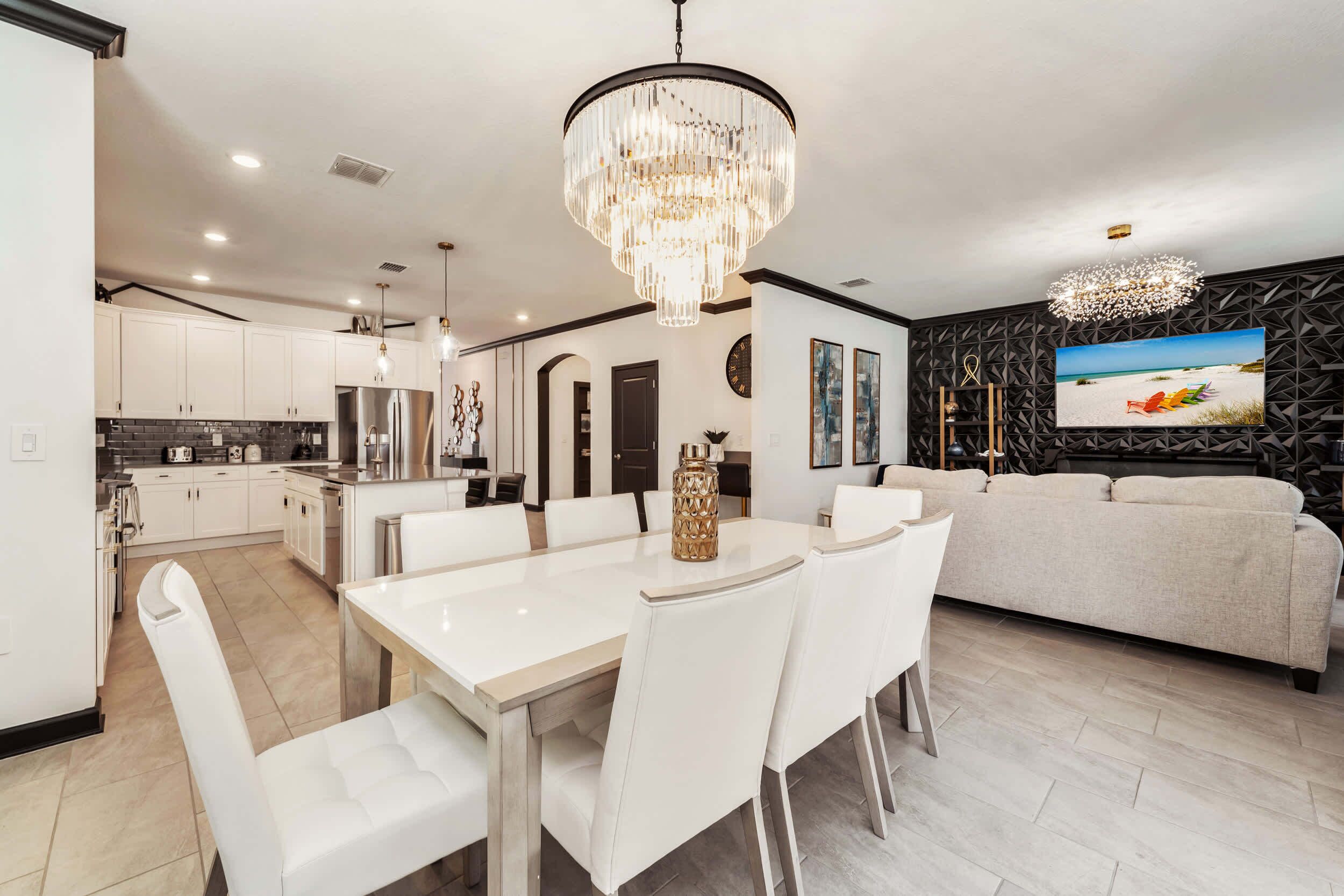 Una cocina moderna con armarios blancos, una mesa de comedor con sillas blancas y una lámpara de araña.