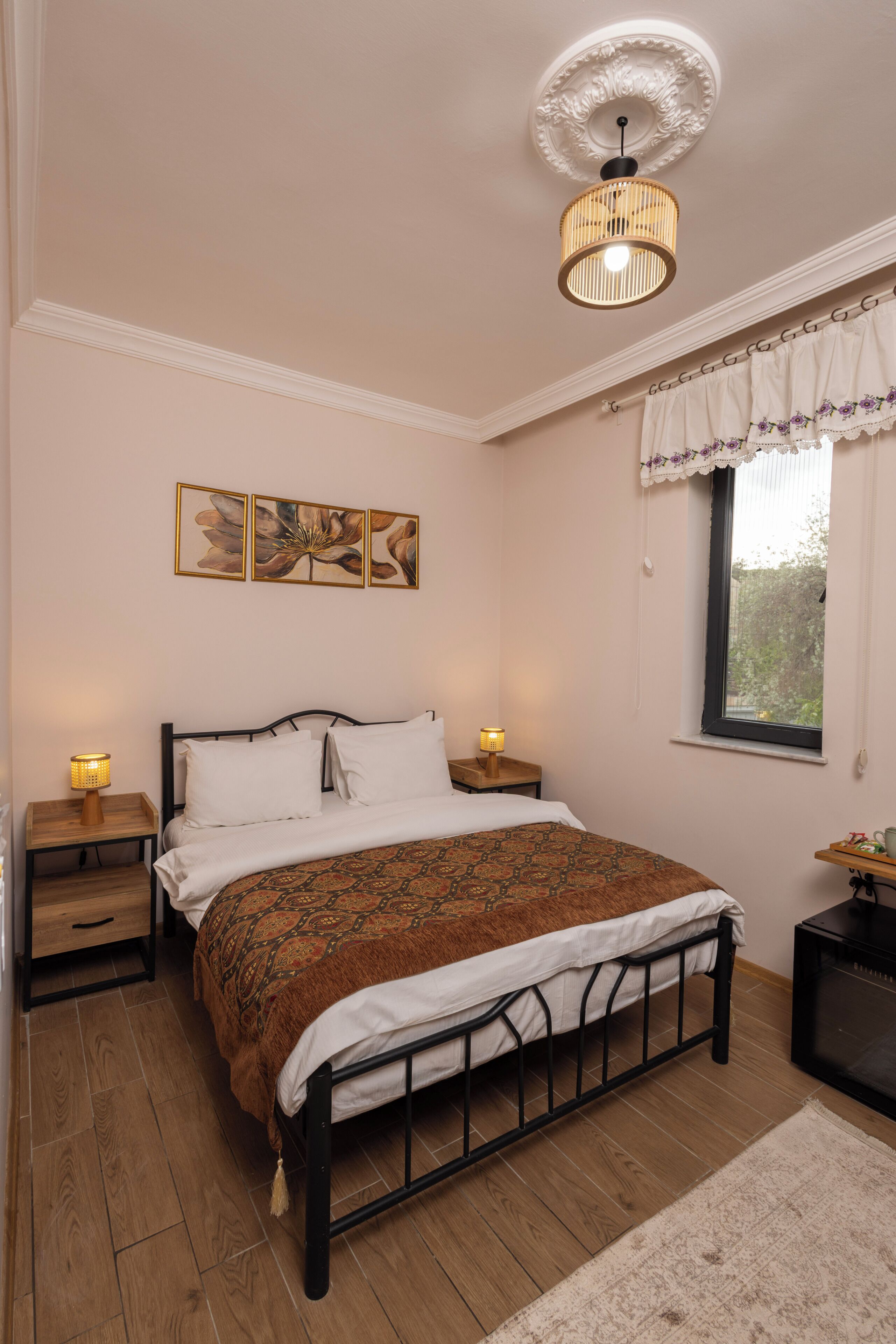 A bedroom with a bed, bedside tables, a window with curtains, a ceiling fan, and wall art.
