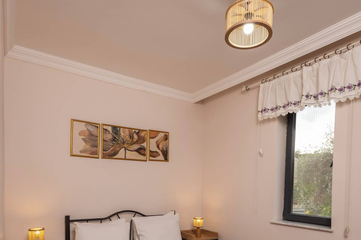 A bedroom with a bed, bedside tables, a window with curtains, a ceiling fan, and wall art.