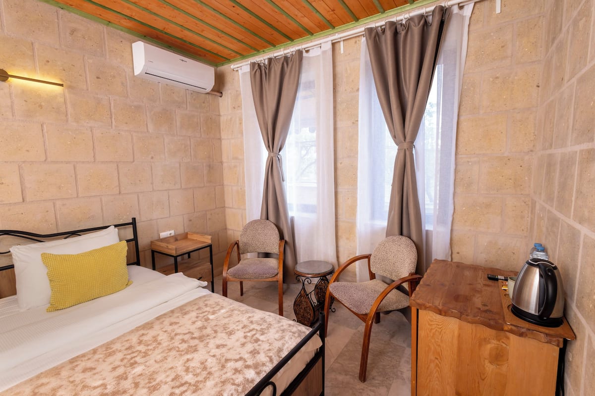 A room with a bed, two chairs, a small table, and a kettle.