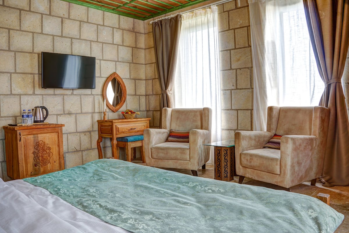 A hotel room with a bed, two armchairs, a wooden desk, a television, and a window with curtains.