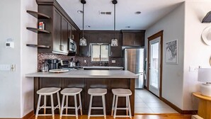 A modern kitchen with dark wood cabinets, a large island with stools, stainless steel appliances, and pendant lighting. - Mission Beach Retreat, Steps to Bay & Beach (San Diego)