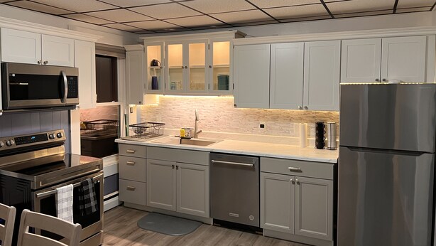 A modern kitchen with stainless steel appliances, light grey cabinets, and a tiled backsplash. - Riverview charming apt near beach (Ipswich)
