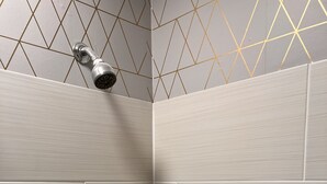 A corner of a bathroom with light grey tiles and a geometric pattern on the wall above the shower area. - Riverview charming apt near beach (Ipswich)