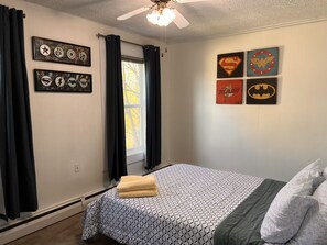 A bedroom with a bed, black curtains, and superhero-themed wall art. - Riverview charming apt near beach (Ipswich)
