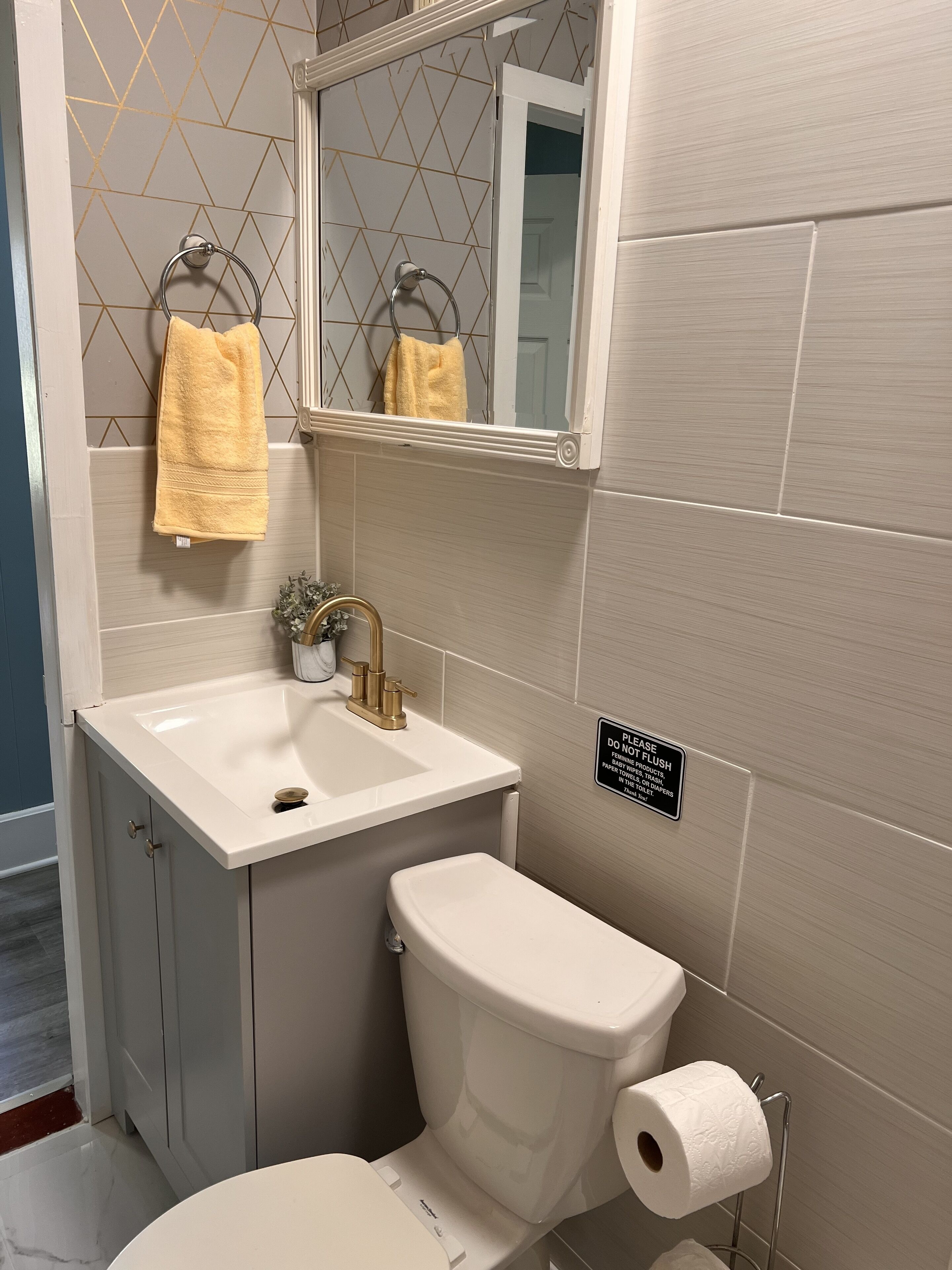 A bathroom with a white sink, gold faucet, and a toilet with a paper towel holder.