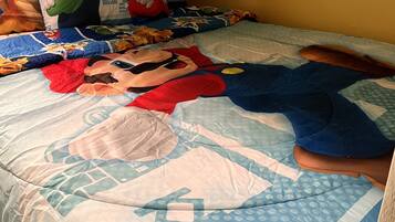 A bedroom with a bed covered in a Mario-themed duvet, a pillow with Mario and Luigi, and a wooden headboard.