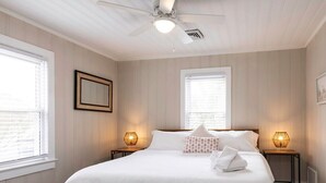A bedroom with a large bed, two bedside lamps, a ceiling fan, and two windows with blinds. - Beachwalk #4, 8 minute walk to the beach (Virginia Beach)