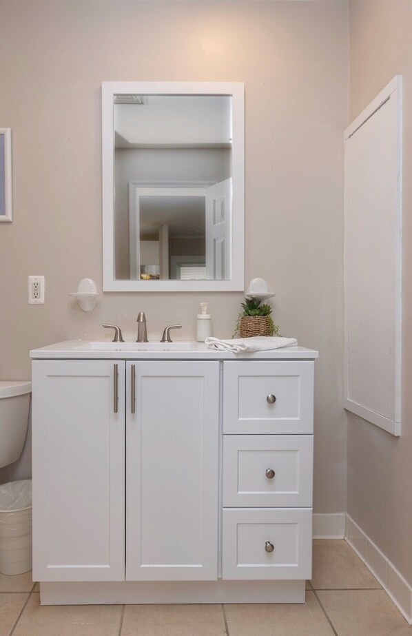 A bathroom with a white vanity, a mirror, a sink, and a toilet.