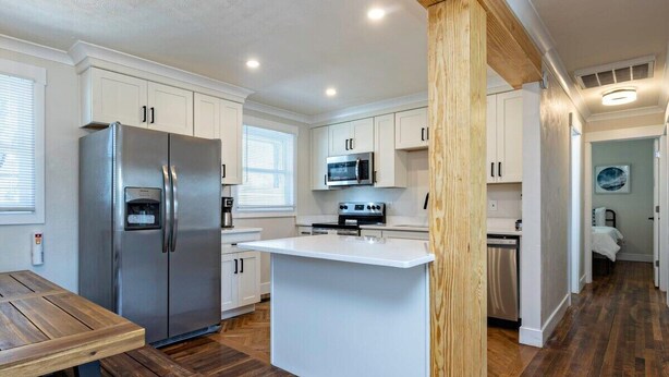 A modern kitchen with white cabinetry, stainless steel appliances, and a wooden dining table. - Beach Vibe with Hot tub! 10 min walk to the Beach! Amazing Backyard! (Virginia Beach)