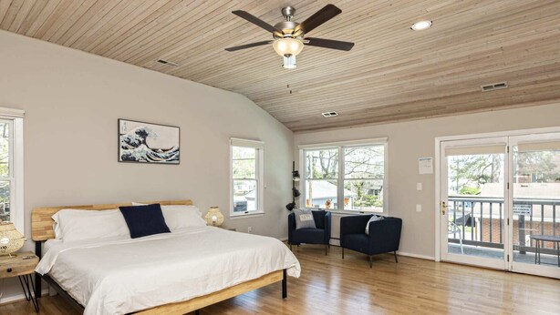A spacious bedroom with a large bed, a ceiling fan, and a view of the outdoors through a sliding glass door. - The VIBE House with POOL! (Virginia Beach)