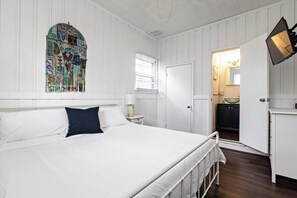 Une chambre à coucher avec un grand lit, une fenêtre décorative en vitrail, une porte blanche donnant sur une salle de bain et une petite table de chevet avec une lampe.