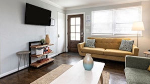 Ein Wohnzimmer mit einer Couch, einem Couchtisch, einem an der Wand befestigten Fernseher und einem Fenster mit Jalousien.
