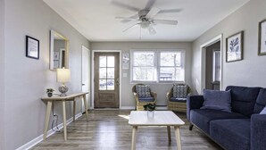 Ein Wohnzimmer mit Deckenventilator, zwei Korbstühlen, einem dunkelblauen Sofa, einem kleinen weißen Tisch und Holzboden.