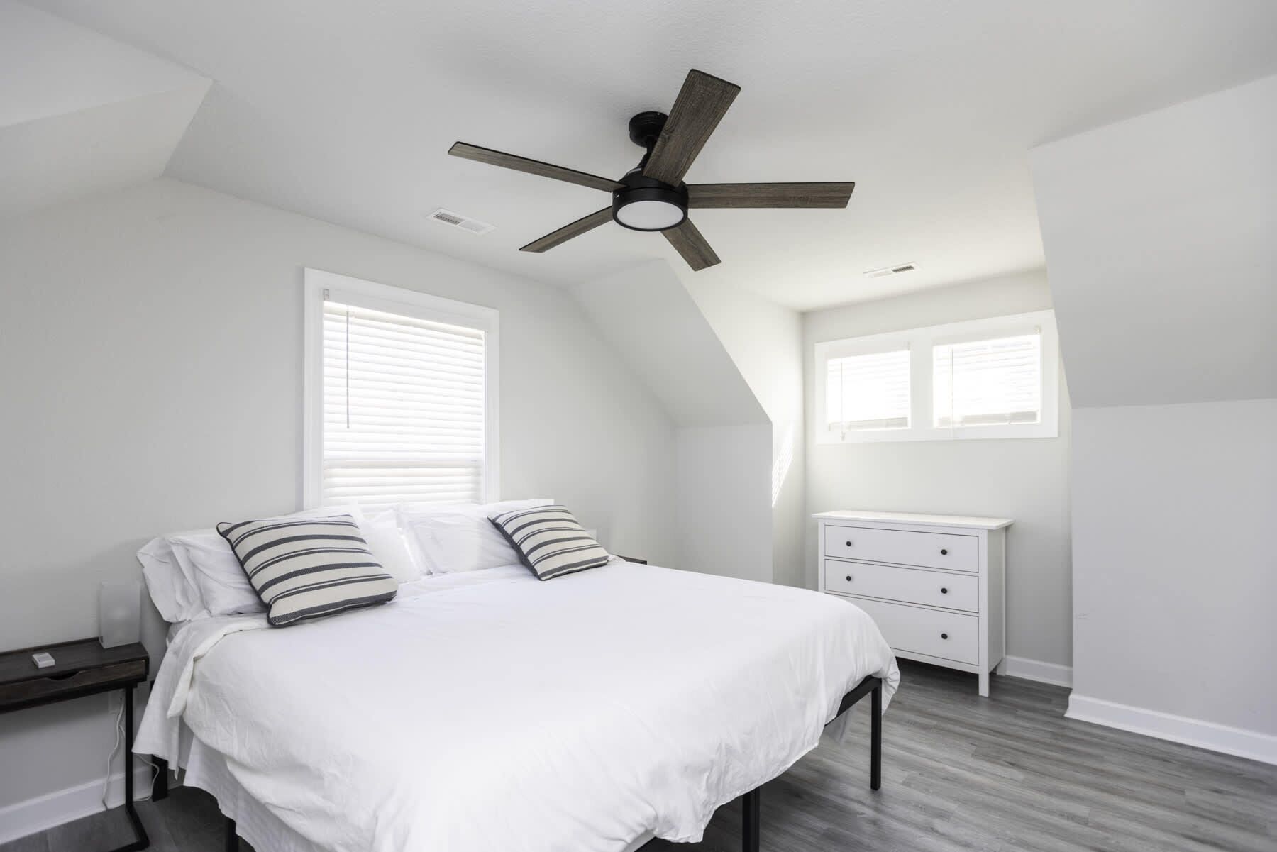 Ein Schlafzimmer mit Bett, Nachttisch, Kommode und Deckenventilator.