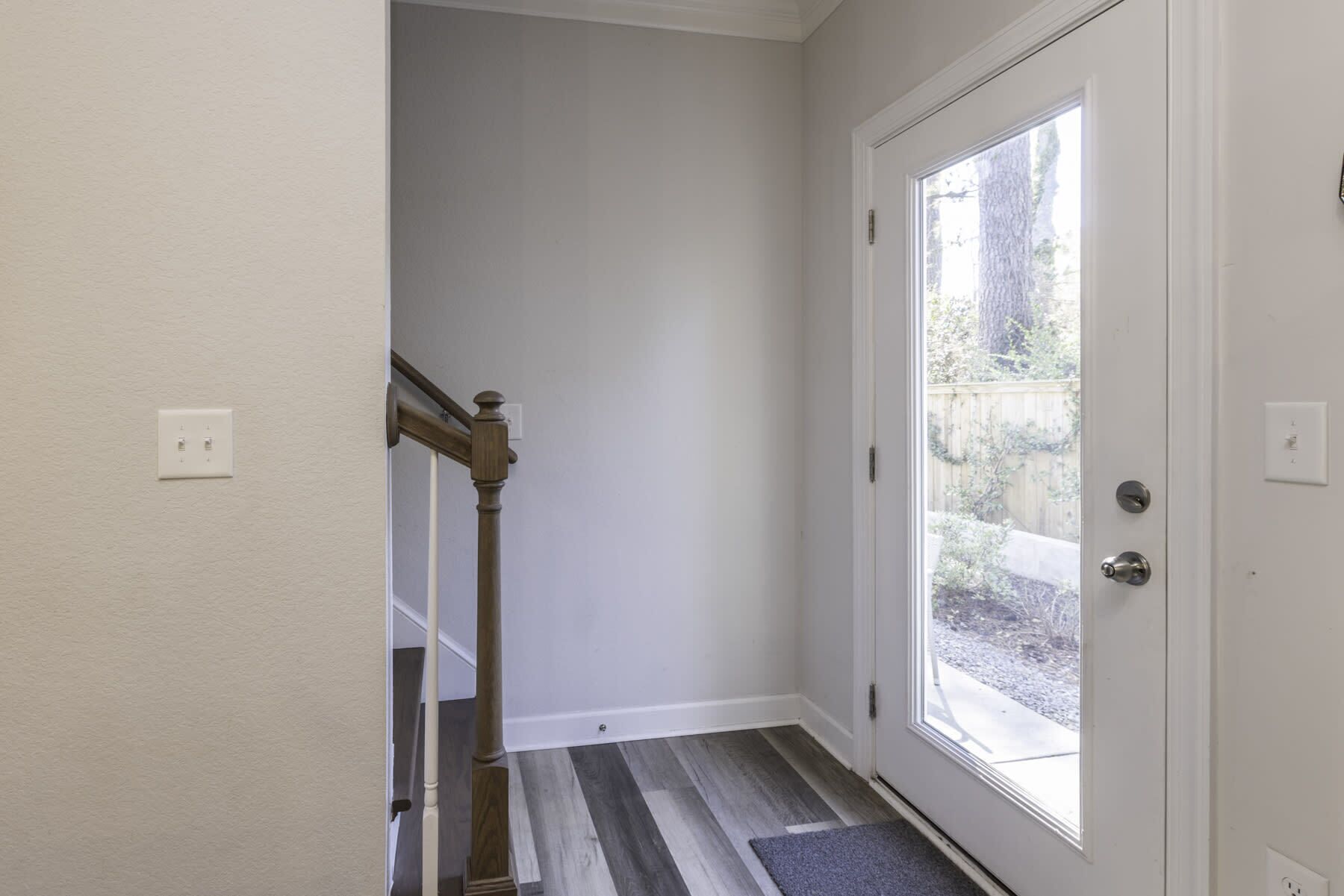 Un couloir avec un escalier en bois, une porte blanche dotée d’une fenêtre et un tapis gris.