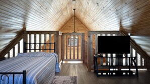 A cozy attic bedroom with a bed, a TV, and a staircase leading to a loft area.