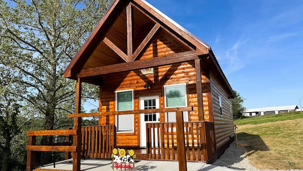 A log cabin with a porch, a welcome sign, and a view of the surrounding landscape.