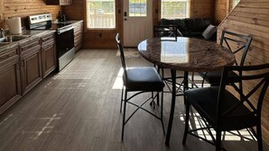 A cozy wooden cabin interior with a kitchen, dining area, and a large window.