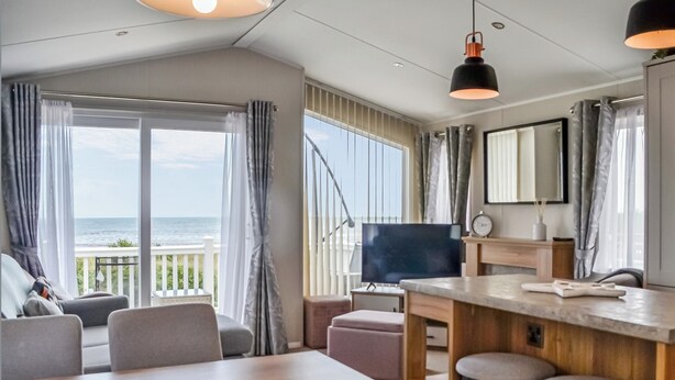 Una habitación moderna con un amplio ventanal con vista al mar, un televisor de pantalla plana, una mesa de comedor de madera y taburetes de bar.