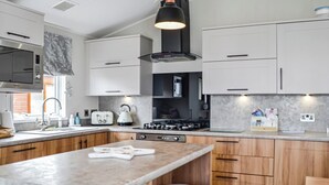 Una cocina moderna con armarios blancos, una isla central con taburetes, estufa a gas y una lámpara colgante negra.