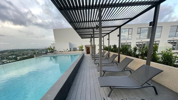 Une piscine sur le toit, avec une terrasse en bois, des chaises longues et une pergola.
