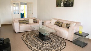 A living room with two sofas, a glass coffee table, a patterned rug, and a painting on the wall. - Kerr Ayo's One Bedroom Apartment, 5 minutes Away from Senegambia Beaches. (Serrekunda)