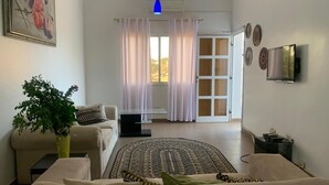 A living room with a sofa, a coffee table, a patterned rug, a potted plant, and a painting on the wall. - Kerr Ayo's One Bedroom Apartment, 5 minutes Away from Senegambia Beaches. (Serrekunda)
