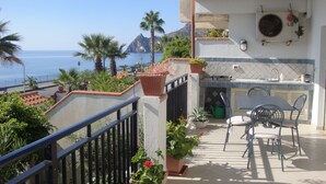 Un balcón con vista al mar, una zona de cocina y mobiliario exterior.