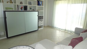 Una sala de estar con un sofá, un mueble con estanterías y un ventanal con cortinas.