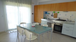 Una cocina moderna con una mesa de vidrio, sillas blancas, armarios de madera y electrodomésticos de acero inoxidable.