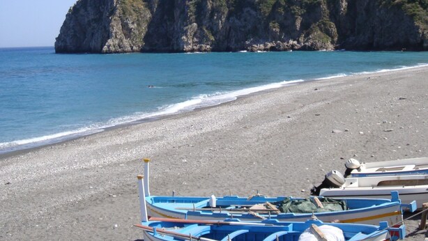 Una playa con barcos y una colina rocosa con una estructura en la cima.