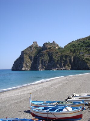 A beach with boats and a rocky hill with a structure on top. - SEAfront Panoramic Terrace, Taormina 10 min drive, free parking and beach (Sant'Alessio Siculo)