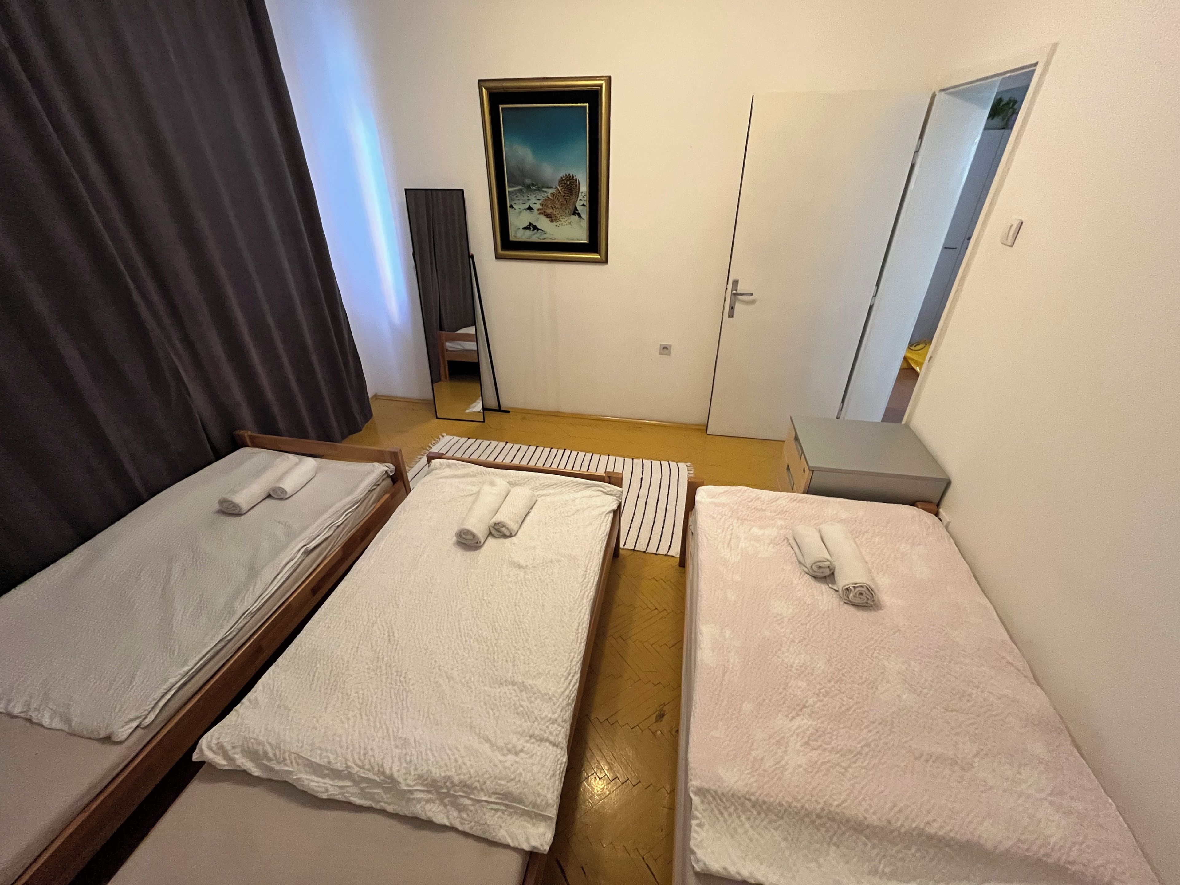 A room with three beds, a mirror, a painting, and a door.