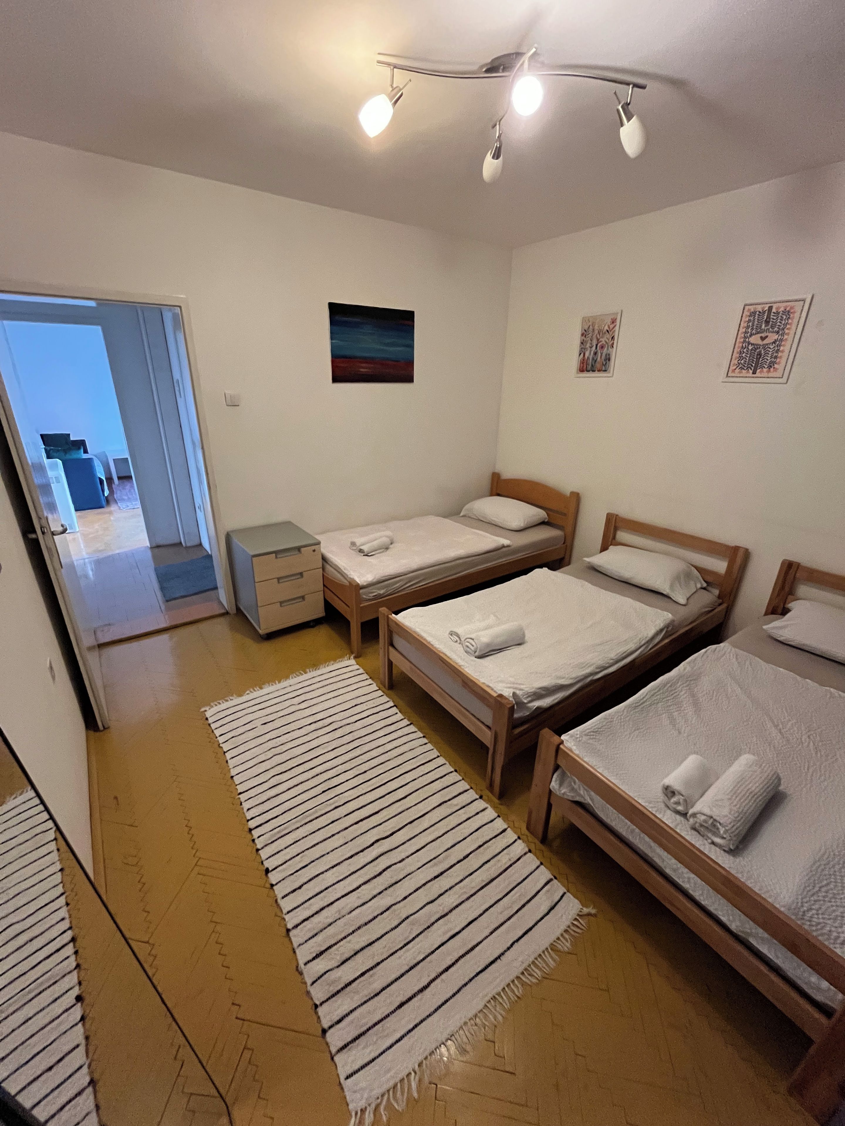 A room with three wooden beds, a striped rug, and a painting on the wall.