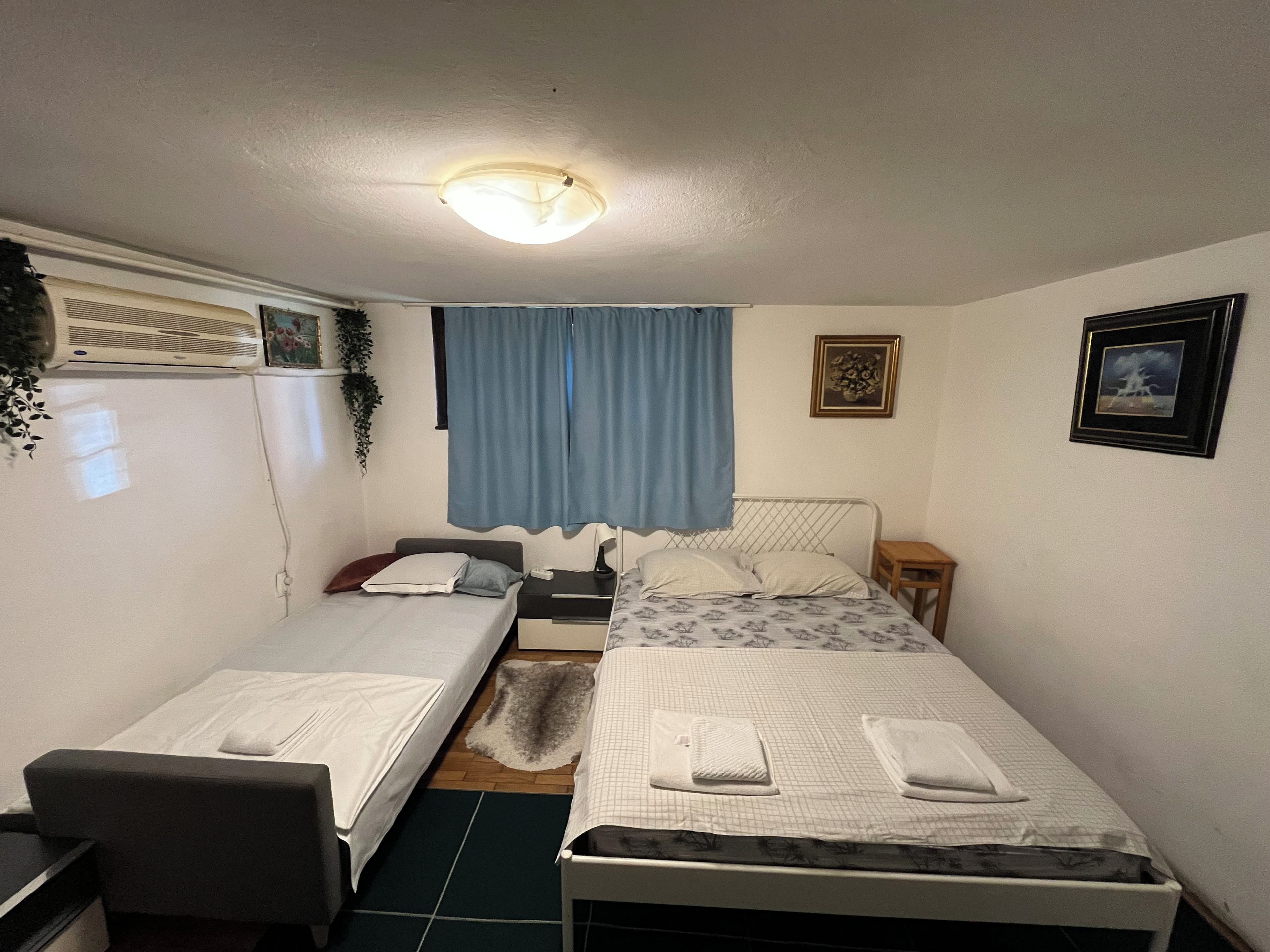 A small, well-lit room with two single beds, a desk, and a chair.