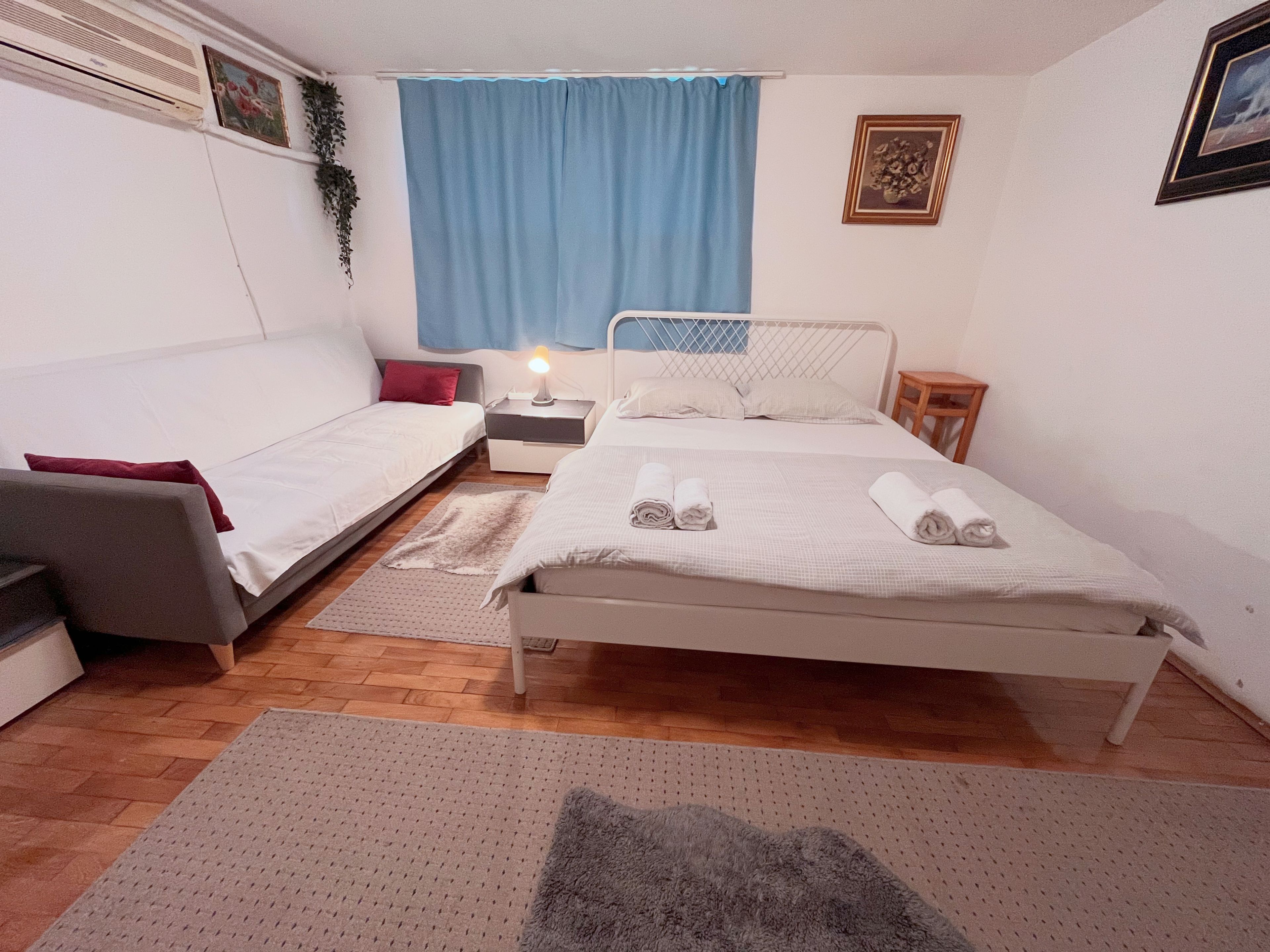 Un dormitorio con cama, sofá, mesita de noche y aire acondicionado de pared.