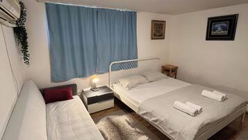 A bedroom with two beds, a nightstand, a lamp, a window with curtains, and a ceiling light.