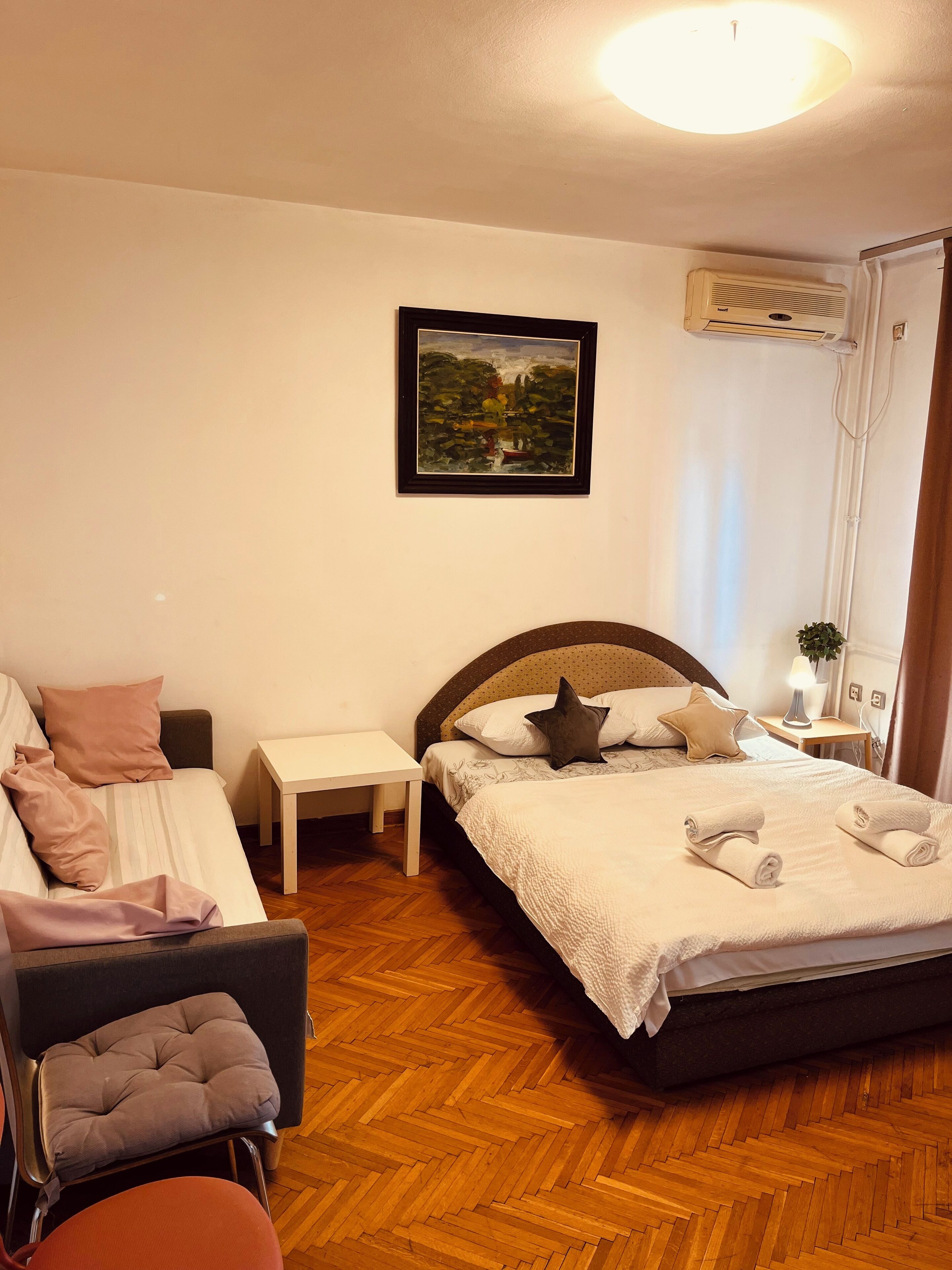 Un dormitorio ordenado con cama, una silla, una mesita y un aire acondicionado de pared.